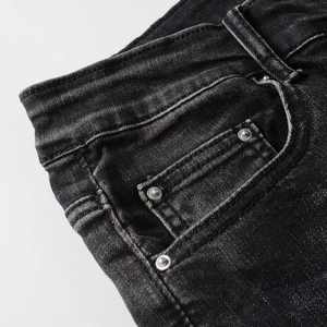 Détail d'un jean slim gris foncé avec des rivets métalliques et texture délavée