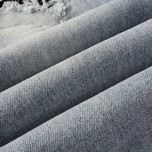 Macro shot of light blue distressed denim fabric with ripped details and twill texture