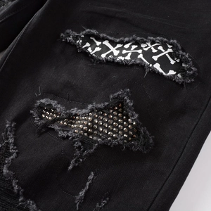Macro detail of men's black distressed jeans with bone patch and silver rhinestones