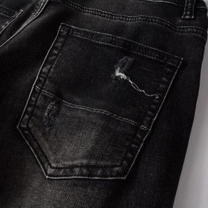 Détail macro du jean slim noir délavé montrant les poches usées et la texture du tissu
