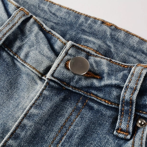 Close-up of high street distressed blue jeans featuring metal button and contrast stitching