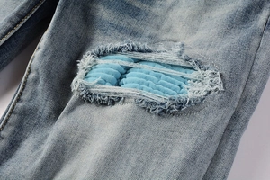 Macro shot of distressed light blue denim with frayed holes and quilted patches