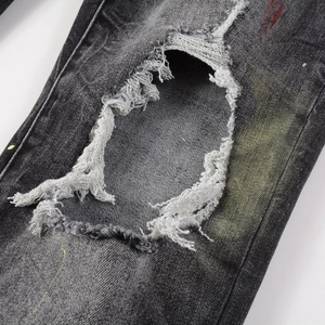 Detail of distressed ripped jeans featuring multi-color paint splatters and frayed edges