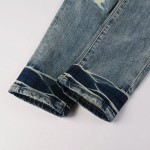 Close-up of blue distressed denim jeans showing orange stitching and washed hem details