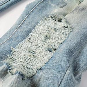 Detail of light blue distressed denim jeans showing vintage ripped holes and inner patches