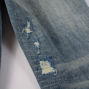 Detailed close-up of vintage blue wash denim with ripped holes and zigzag stitching detail