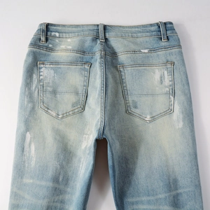 Detail of light blue washed denim jeans with white paint splatter and distressed back pockets