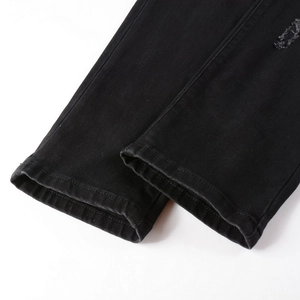 Detail of distressed hem and frayed edges on black slim-fit denim jeans for men