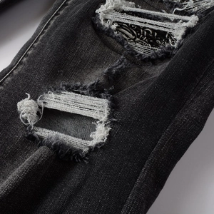Détail d'un jean noir vieilli avec texture déchirée et écussons imprimés au style unique