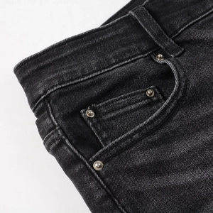 Macro shot of dark grey denim jeans featuring reinforced stitching and silver metal rivets