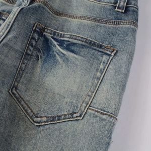 Detail of blue wash denim jeans back pocket featuring orange stitching and distressed fabric