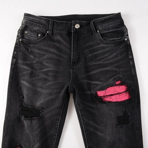 Détail du jean slim noir usé avec doublure en maille rose sous les trous du denim déchiré