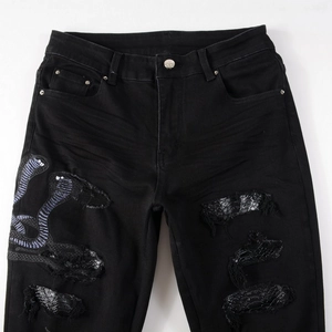 Detail of street style black slim jeans with cobra embroidery and snakeskin leather patches
