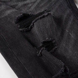 Detail of black slim fit jeans showing heavy distressed ripped holes and denim texture