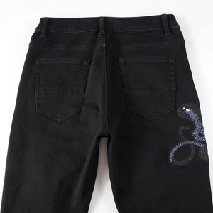 Detailed embroidery of a purple cobra on black distressed stretch denim jeans for men