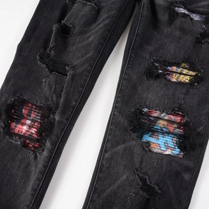 Detail of distressed black denim jeans featuring colorful graffiti and plaid fabric patches