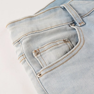 Nahaufnahme von Metallnieten und gelben Nähten auf hellblauen Distressed-Denim-Jeans