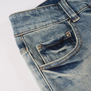 Detail of blue distressed denim showing metal rivets, slanted pockets, and vintage stitching