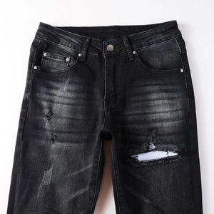 Detailed view of black distressed denim jeans with frayed holes and washed cat whiskers