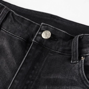 Détail macro du bouton métallique argenté et passants sur un jean noir délavé