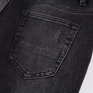 Detailed close-up of the back pocket on slim fit black denim jeans with embroidery