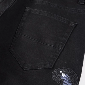 Detail of black distressed denim pocket with premium purple cobra embroidery stitching