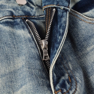 Close-up of metal zipper fly and silver button on blue washed distressed denim jeans