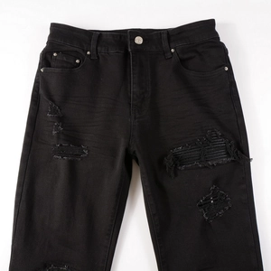 Detailed view of black slim fit denim with distressed knee rips and washed texture