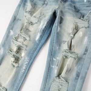 Distressed light blue slim fit jeans with heavy rip details and white paint splatters