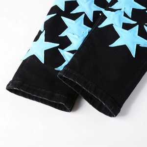 Dettaglio dei jeans neri stile street con toppe a stella azzurre e cuciture rifinite