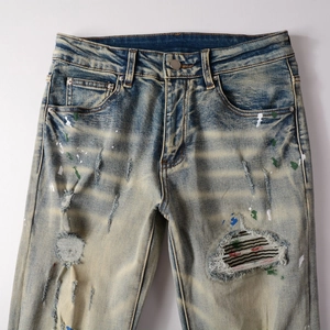 Detail of distressed blue denim jeans with paint splatters, rips and vintage wash finish
