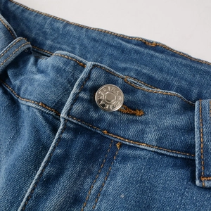 Macro shot of blue denim jeans waist with metal button and orange contrast stitching