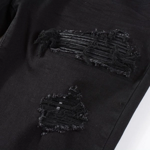 Detailed view of black distressed denim with ripped design and leather inner patch