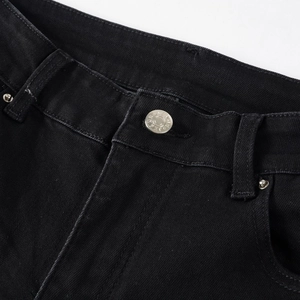 Close-up of black denim waist with embossed metal button and reinforced rivet detailing