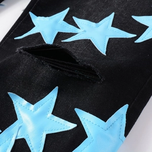 Dettaglio delle toppe a stella in pelle azzurra e strappi usurati su jeans in denim nero