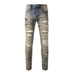 Gros plan d'un jean bleu slim avec broderie serpent et détails déchirés avec empiècements