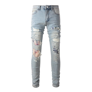 Detail of light blue slim fit jeans featuring distressed holes and colorful patchwork inserts
