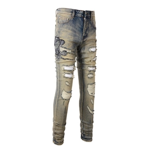 Détail du jean slim avec délavage vintage, broderie cobra et déchirures sur les jambes