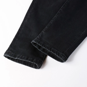 Detailed view of double-stitched hem and fabric texture on black slim-fit denim jeans