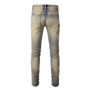 Détail macro du jean slim vintage pour homme avec délavage jaune et broderie serpent au dos
