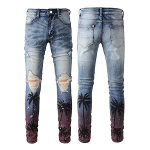 Detail of ripped blue slim-fit jeans featuring palm tree silhouettes and sunset gradient print