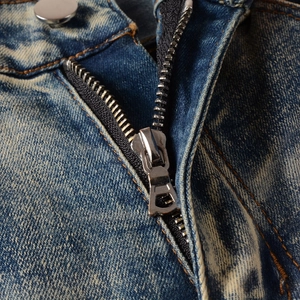 Detail of silver metal zipper and button on blue vintage washed high-street denim jeans