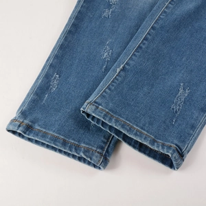 Detail of distressed medium blue denim jeans hem with orange stitching and rip effects
