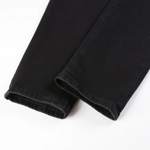 Detail view of double-needle hemmed cuffs on men's black slim-fit stretch denim jeans