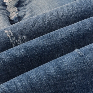 Detailed close-up of blue denim fabric with distressed holes and raw edge embroidery