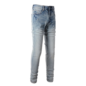 Detail view of light blue slim fit denim jeans with distressed whiskers and small rip