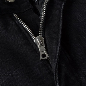 Macro shot of silver metal zipper and black twill fabric detail on distressed jeans