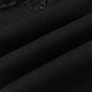 Detailed macro view of black twill denim fabric texture and distressed ripped design