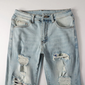 Detail view of light blue distressed jeans with frayed denim rips and metal button accents