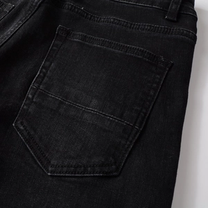Detailed close-up of the back pocket on black distressed denim pants with double stitching